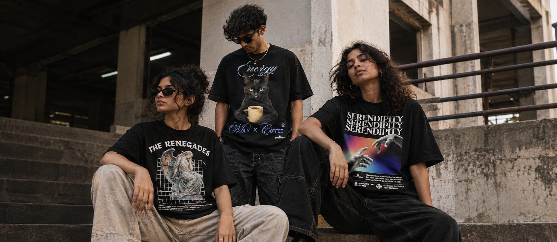 Three friends on the concrete steps of an industrial stairwell in black Bean Brew tees: The Renegades, Energy (Milk x Coffee) and Serendipity